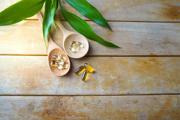 Natural vitamins and supplements in wooden spoons on wood table with leaf blackground.