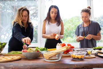 Attractive women preparing healthy meal. Beautiful young women in sportswear standing near table and cooking fresh organic vegetables. Healthy eating concept