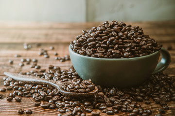 Cup full of Black coffee grains lie on a brown wooden table, background image. Coffee beans in a green cup.