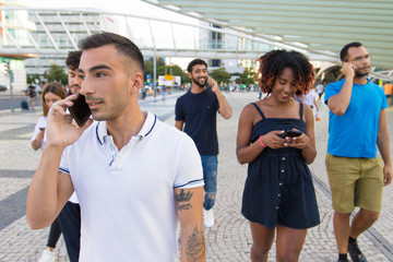 Diverse group of people excited with their smartphones. Mix raced men and women walking outside,...