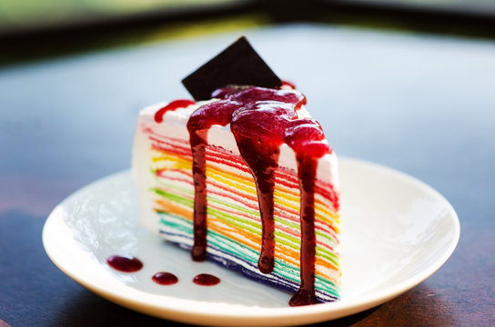 closeup of colorful rainbow crape cake on white plate , serving with strawberry sauce topping