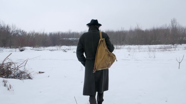 A traveler in a hat walks through a snowy field