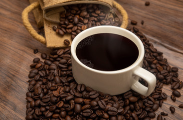 Cup of coffee beans and burlap sack on wooden background, copy space banner