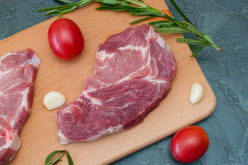 Raw meat pork steak with tomatoes garlic and rosemary on a wooden cutting board close-up, top view
