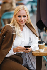 Image of smiling woman using mobile phone and drinking coffee