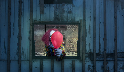 A clown with a balloon looks out of a window