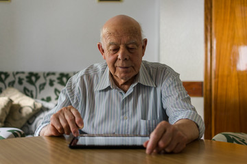 Elderly man is using a digital tablet at home