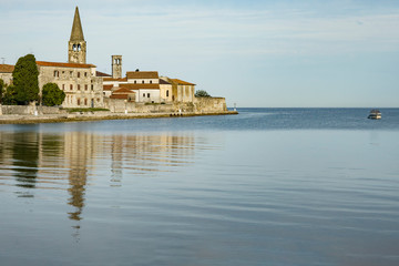 Fototapeta na wymiar Ancient stone town located on the Peninsula. The city is surrounded by the sea, ancient buildings reflected on the water. Istria, Croatia, Porec.