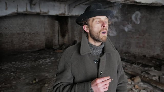 Bearded man in a hat lets out rings of cigarette smoke