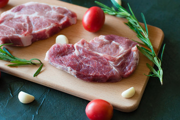 Pork steaks raw, red tomatoes, rosemary and garlic on a cutting board