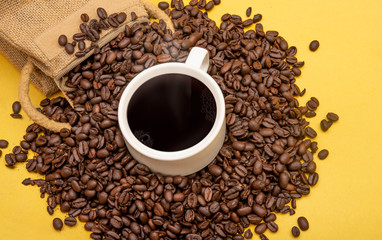 Cup of coffee beans and burlap sack on yellow background, copy space banner