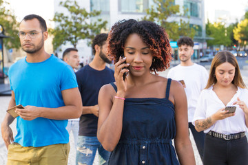 Diverse group of people using their smartphones while walking down street. Mix raced men and women walking outside, talking on cells, using mobile phones. Mobile connection concept