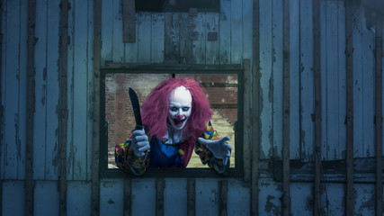 a bad clown with a knife looks out of a window