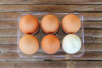 close up Six brown eggs in plastic box on bamboo table with one broken boiled egg, top view.