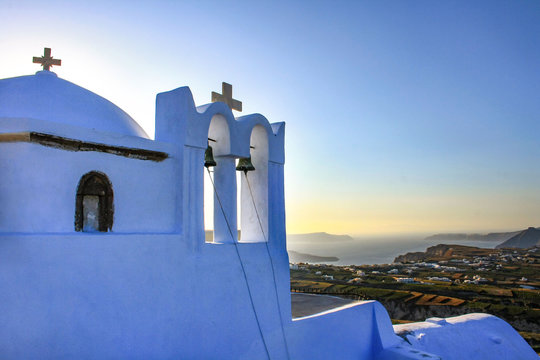 Biała dzwonnica i kości&oacute;ł w Pyrgos, w tle morze i  panorama greckiej wyspy Santorini