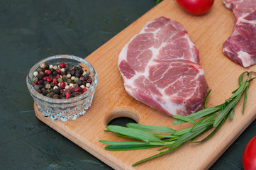 Raw meat steaks, red tomatoes, rosemary and peppers on dark background