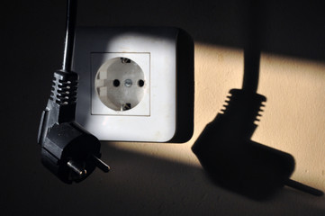 wall outlet with a hanging plug in the sunlight. The plug is out of focus.