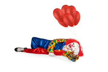 Fototapeta na wymiar A cheerful clown lies on the floor holding balloons in his hand