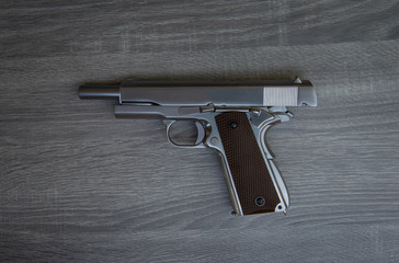 Stainless hand gun with brown hand grip is on the wooden floor