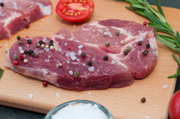 Piece of raw pork meat sprinkled with pepper and salt with chopped tomato and rosemary, process of cooking steak