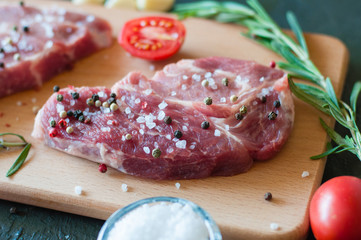 Piece of raw pork meat sprinkled with pepper and salt with chopped tomato and rosemary, process of cooking steak