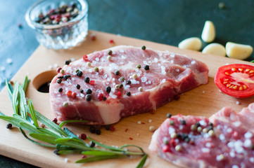 Raw pork meat sprinkled with pepper and salt with chopped tomato garlic and rosemary, steak cooking process