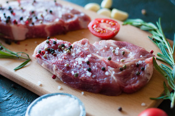 Raw pork meat sprinkled with pepper and salt with chopped tomato garlic and rosemary, steak cooking process