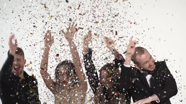 Medium shot of happy young men and women laughing and throwing confetti up in the air, then dancing as its falling down on them from above