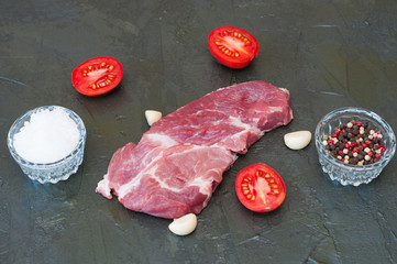 Flat lay, cooking process of pork steak, salt, pepper, garlic and sliced tomato on gray concrete background