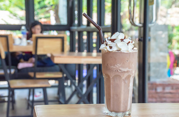Cold cocoa with whipped cream on top of the glass on wooden table Background glass windows and  tree.