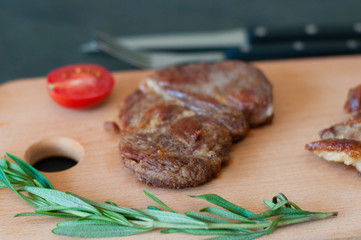 Grilled veal, beef or pork steak, tomato, rosemary and soy sauce for meat, knife and fork, on a wooden board, close-up