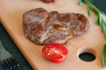 Grilled veal, beef or pork steak, tomato, rosemary and soy sauce for meat, knife and fork, on a wooden board, close-up