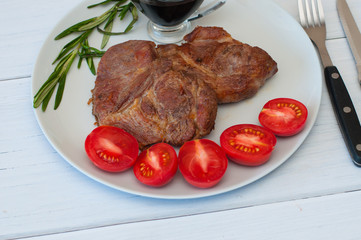 Tasty, grilled pork steaks on a gray plate with sauce, rosemary and tomatoes, on light wooden background, cutlery, close-up