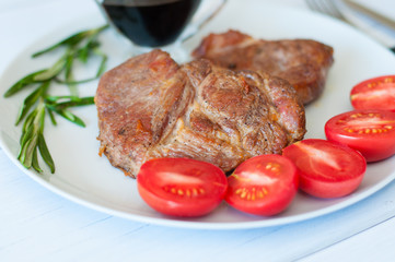 Tasty, juicy, fried meat steaks of pork or beef with sauce, spices and tomato on gray plate on a light background