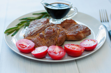 Fried, very tasty and juicy meat steaks of pork or beef with sauce, spices and tomatoes, on a gray plate, on light wooden background