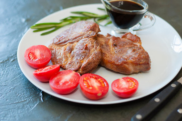 Fragrant pork meat steaks with spices, tomatoes and sauce, on a gray plate, on dark concrete background with place for text