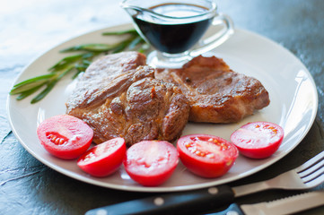 Fragrant, juicy meat steaks of veal, beef or pork with rosemary, tomatoes and sauce, on gray plate, on a dark concrete background