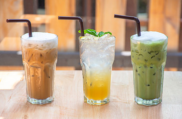 Iced Coffee, Honey Lemon Soda  and strawberry smoothie in glass on the wooden table Background glass windows and  tree.