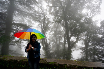 Young indian girl with a colorful umbrella standing in front of spooky foggy trees