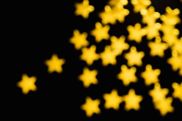 Defocused golden decorative stars on black background. Abstract backdrop. Festive , party and holiday concept.