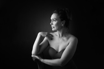 Portrait of a sensual fifty year old woman on grey studio background. Monochrome shot.