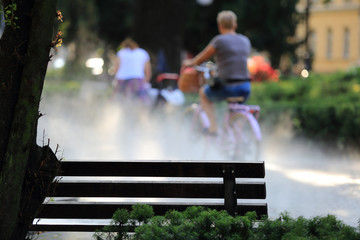 Ławka w parku i kobieta na rowerze, mgła.