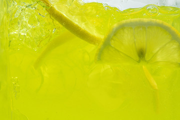 Close up view of the lemon slices in lemonade background. Texture of cooling sweet summer's drink with macro bubbles on the glass wall. Fizzing or floating up to top of surface.