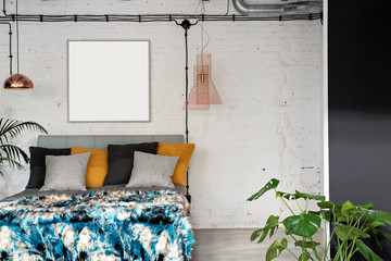 Interior of bedroom in loft apartment with double bed with pillows and gold  and modern lamps. Brick wall with frame with mock up. Industrial and scandinavian style.
