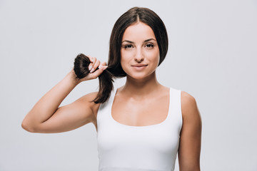 brunette beautiful woman holding long straight healthy and shiny hair isolated on grey