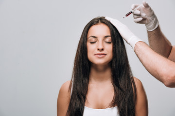 cosmetologist in latex gloves doing scalp mesotherapy to brunette beautiful woman with long hair and closed eyes isolated on grey - obrazy, fototapety, plakaty