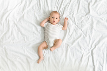 Cute baby in bodysuit lying on bed, looking to camera