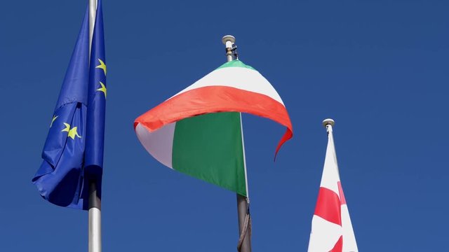 Slow motion of some flag, Italian flag and European flag. Clear blue sky, zoom in shot.