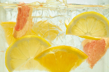 Close up of lemon and grapefruit slices in lemonade and ice cubes background. Texture of cooling...