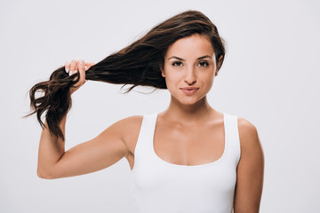 smiling brunette beautiful woman holding long healthy and shiny hair isolated on grey
